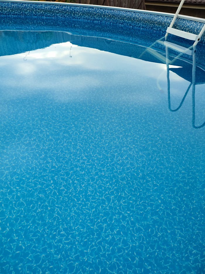 heros-img Captivating view of a blue swimming pool with a ladder reflected on the surface, ideal summer relaxation spot.