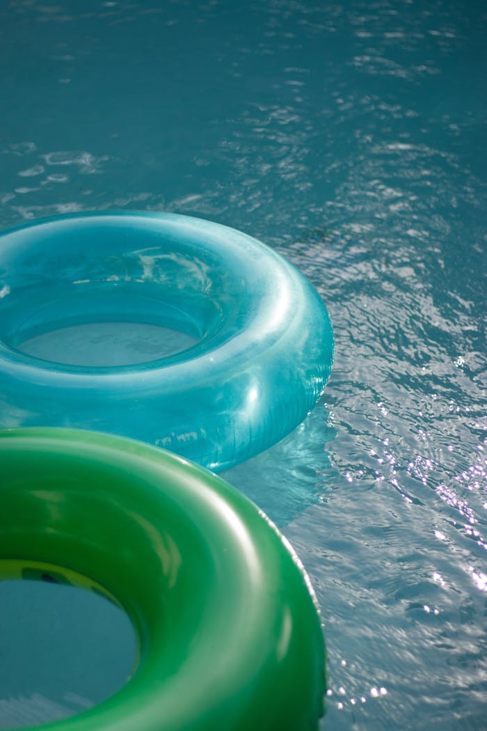 about-us-01 Blue and green inflatable pool rings floating on a shimmering swimming pool surface.